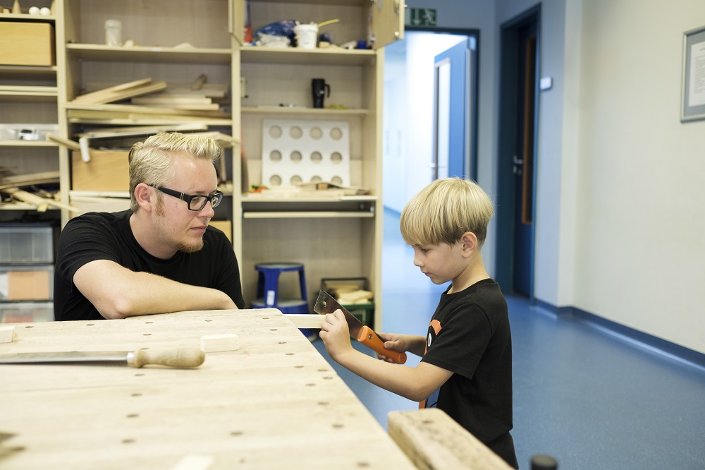 Mann hilft Kind beim Holzsägen
